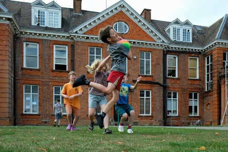 Children playing with a ball on a lawn outside a large red brick house