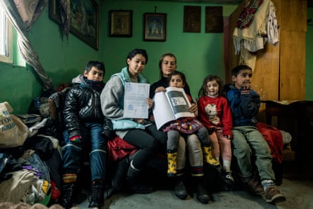 A woman and five children sit in a small room. One of the children holds a document; the woman holds a photocopy of an ID card