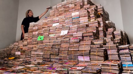A woman beside a vast stack of postcards sent in to Post Secret.