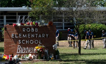 a group of people in blue shirts search the grass near a red brick sign