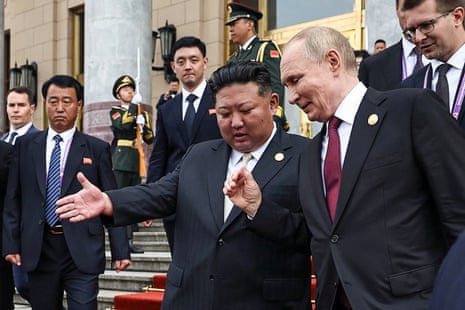 Vladimir Putin and Kim Jong-un speak and gesture with their hands on the steps, surrounded by aides