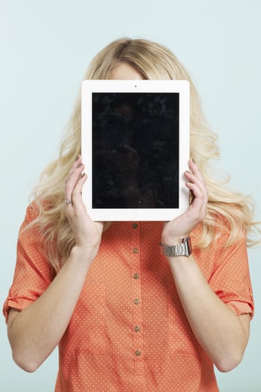 A women hides her face behind a tablet computer