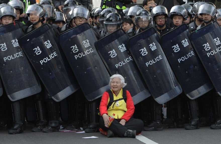 A woman sits in front of riot police blocking the road to protect protesters during an anti-government march on 24 April 2015 in Seoul, South Korea.