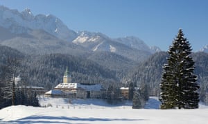 A snowy scene of Schloss Elmau Castle Hotel with forest and Wetterstein mountain range behind