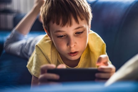 A boy looks at a mobile phone while laying on a couch