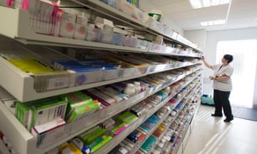 A female pharmacist at work: she is seen in white overalls stacking a set of long shelves filled with medicines