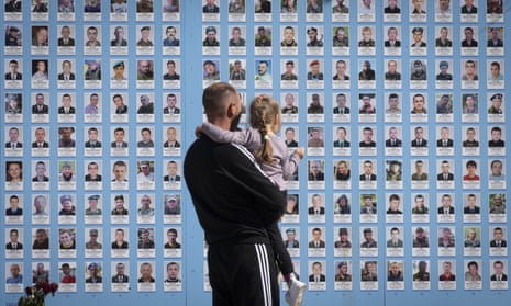 A man holds his child at the Memorial Wall of Fallen Defenders of Ukraine which shows photos of his killed fellow soldiers in Kyiv, Ukraine, on Thursday, September 8. (AP Photo/Efrem Lukatsky)