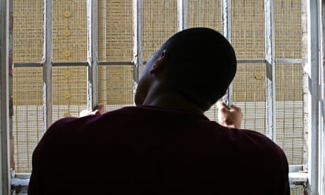 A young black prisoner looks out through the bars of his cell window