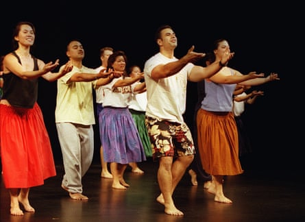 Seven people dance hulu in casual outfits on a darkened stage.