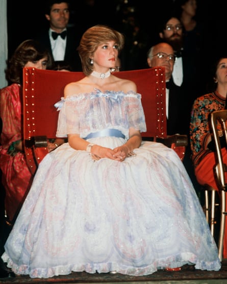 Diana seated in a flowing white dress with shoulderless sheer top and blue ribbons