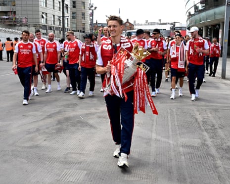 Martin Ødegaard carries the Premier League trophy to the open-top bus outside the Emirates Stadium