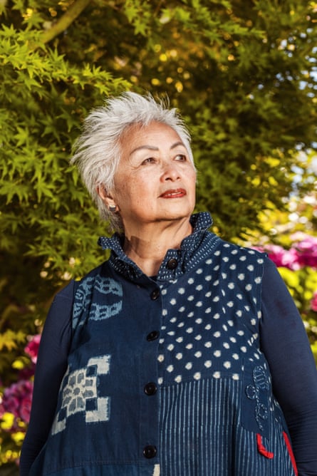 Woman with shock of white hair and stylish denim dress looks to the side.