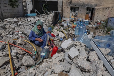 An elderly woman sits on top of rubble of a destroyed house.