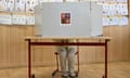 A woman sits behind a screen at a voting booth