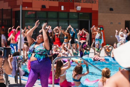 A crowd of merfolk claps and dances at the poolside. 