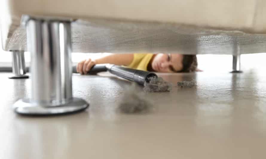 A woman reaching under a sofa to vacuum some dust