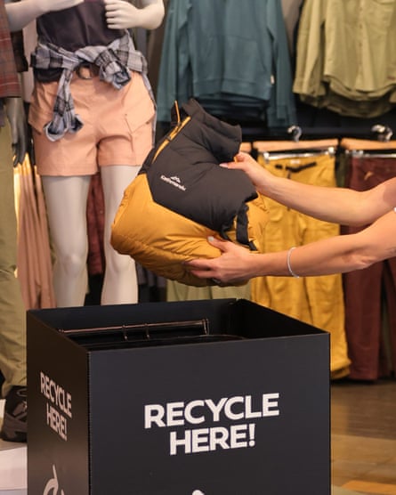 A Kathmandu-brand black and yellow backpack being placed into a clothing donation bin in a Kathmandu store.