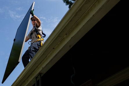 a man holds a solar panel on the roof of a home