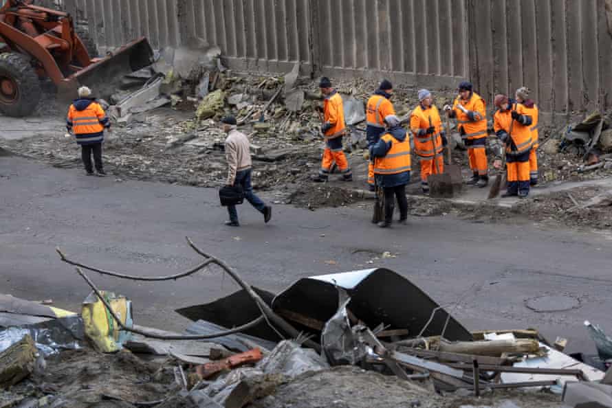 A local resident walks past the site of the missile strike as workers look through the rubble.