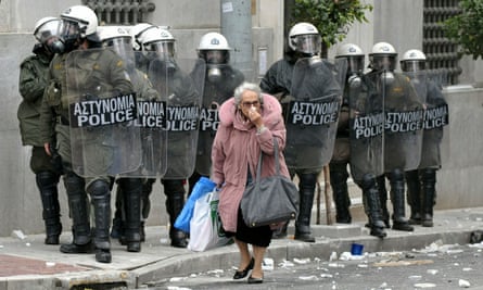 A woman walks past riot police during clashes with protestors December 15, 2010 in Athens, Greece.