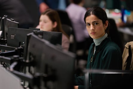 A smartly dressed woman looks quizzical as she sits behind her computer monitor in a busy office