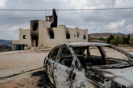 A burnt-out car sits before a scorched, smoke-stained house in Jalud, West Bank