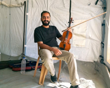 Seated bearded man in a tent holding a violin and bow