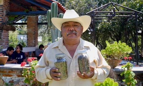 Portrait of Mexican farmer Isidro Cisneros holding two glass jars filled with cannabis produce.