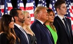 Six white men and women stand in a line in front of a row of American flags, with everyone dressed in black and dark blue except Melania, who wears a lime green dress.