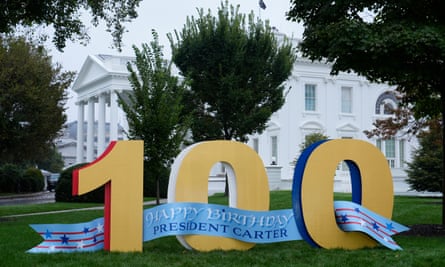 A blue banner saying ‘Happy Birthday President Carter’ loops through large yellow ‘100’ numbers on the grass in front of the White House