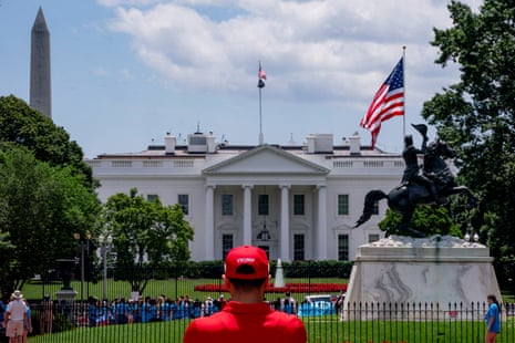 A man in a red outfit and hat stands before a large white building