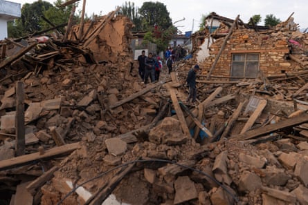 A small group of people stand in the collapsed remains of a completely destroyed house