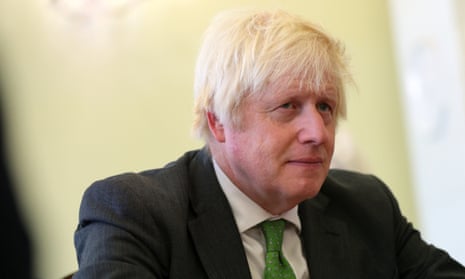 Boris Johnson photographed at Lviv National University, Ukraine, September 2023 – close-up of him sitting against pale yellow backdrop the same colour as his hair, wearing dark jacket, white shirt and green tie