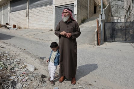 Fahed Ahmaro stands holding hands with a small boy on a debris-strewn street