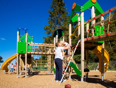 Father helping his toddler son get down off play equipment at an adventure playground