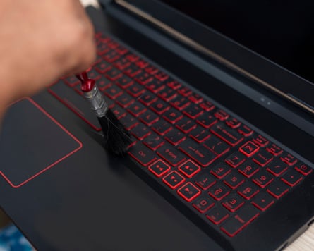 A computer technician removes dust from the keypad of a laptop with a brush. Laptop maintenance and cleaning.