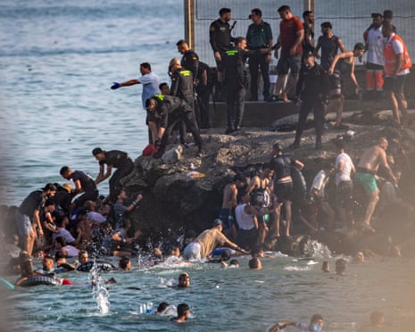People climb out of the sea on to a rocky shore