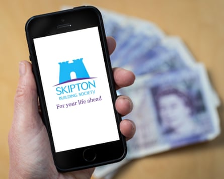 A hand holding a smartphone with the Skipton building society logo on the screen