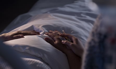 A posed image of a terminally ill patient lying in bed and an assisting family member holding their hand