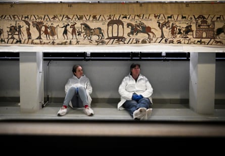 Two people sit under the Bayeux tapestry.