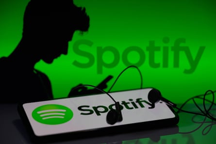Silhouette of a person next to Spotify logo and with logo also on a phone with earphones in the foregrund