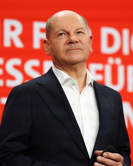 Olaf Scholz standing in front of a red backdrop