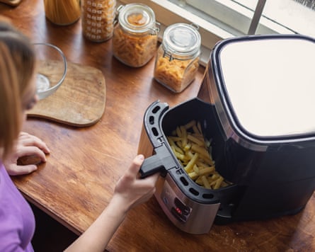 A teenage girl using an air fryer in the kitchen to prepare french fries