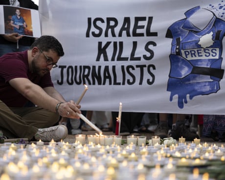 A man lights a candle in frint ot a banner that reads 'Israel kills journalists'