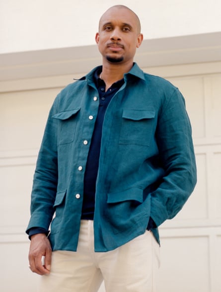 Thomas J Price, with a moustache and goatee and wearing an overshirt with four big pockets, stands with one hand in his jeans pocket