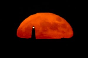 A full moon rises behind the Boston Light, in Winthrop, Massachusetts, US