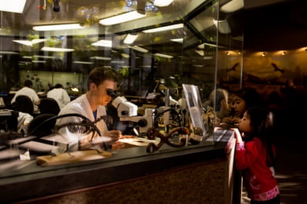 A man looking into a microscope while a young girl looks at him