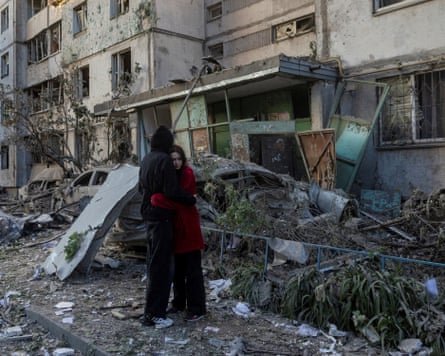 Two teenagers hug outside a damaged building