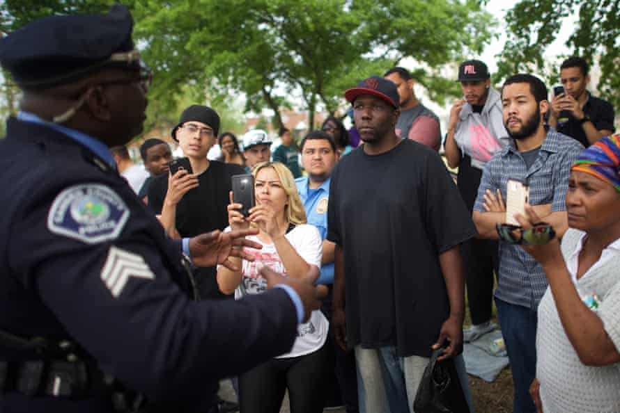 Neighborhood residents film a police officer with cellphones while speaking about police mistreatment in Camden, New Jersey, on 18 May 2015.