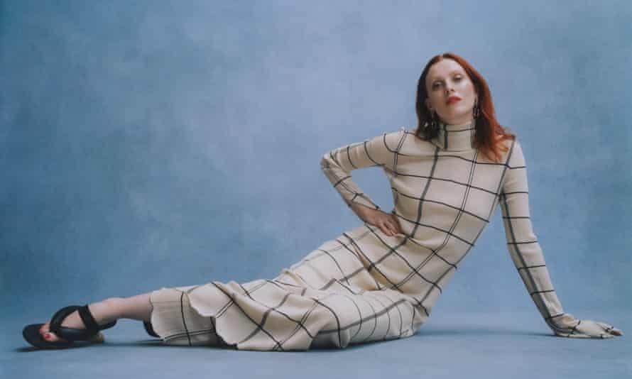 Model Karen Elson in checked dress, sitting on floor, against blue background